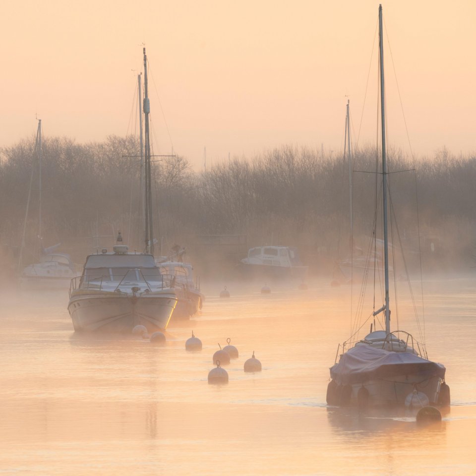Boats moored on a misty river at sunrise.