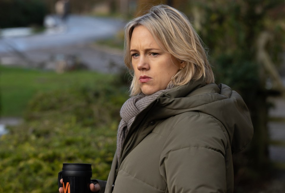 A woman in a green jacket and gray scarf holds a travel mug.