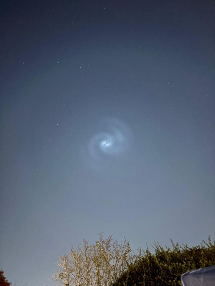 Spiral cloud formation in night sky above trees.