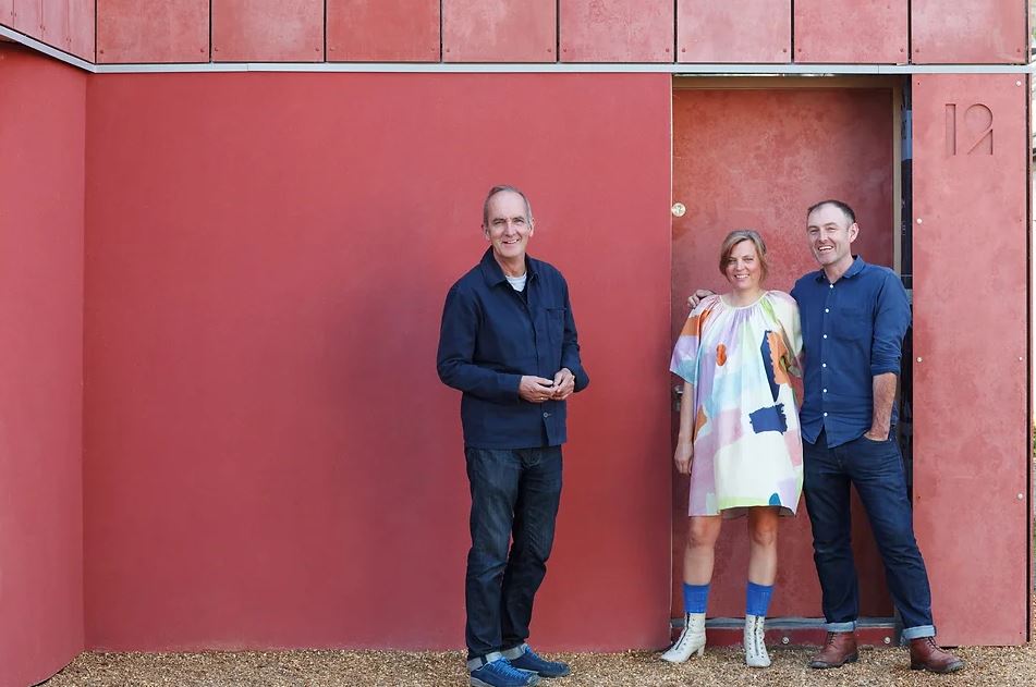 Three people stand in front of a red wall.