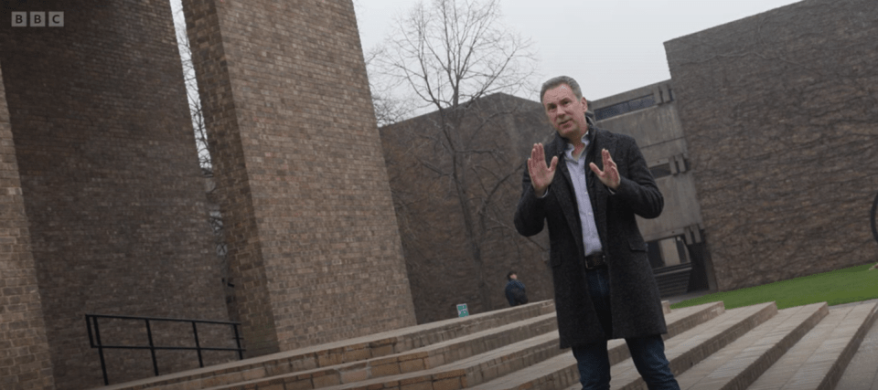 Man gesturing in front of a brick building.