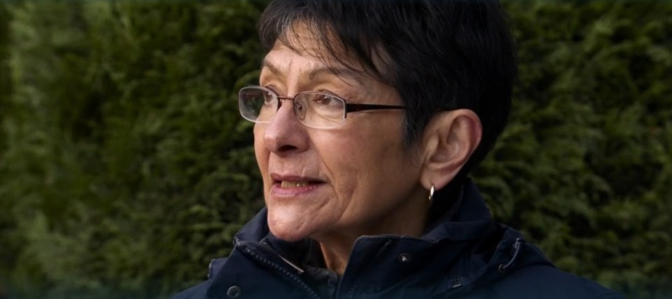 A woman wearing glasses speaks outdoors.