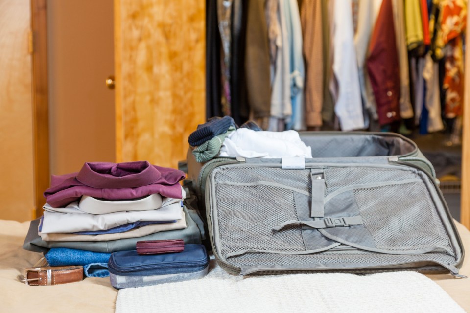 Open suitcase with clothes packed inside and folded clothes on a bed.