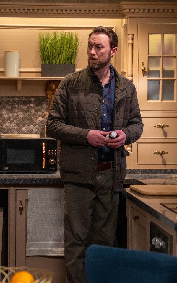 Liam Cavanagh checking Chas Dingle's pill consumption in a kitchen.