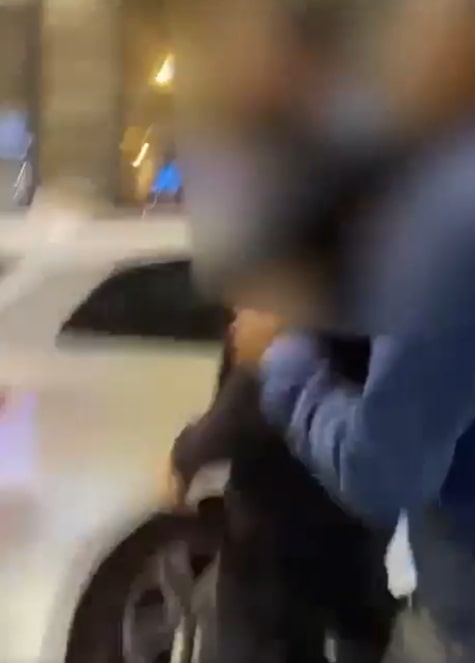 Blurry image of a person being apprehended near a car.