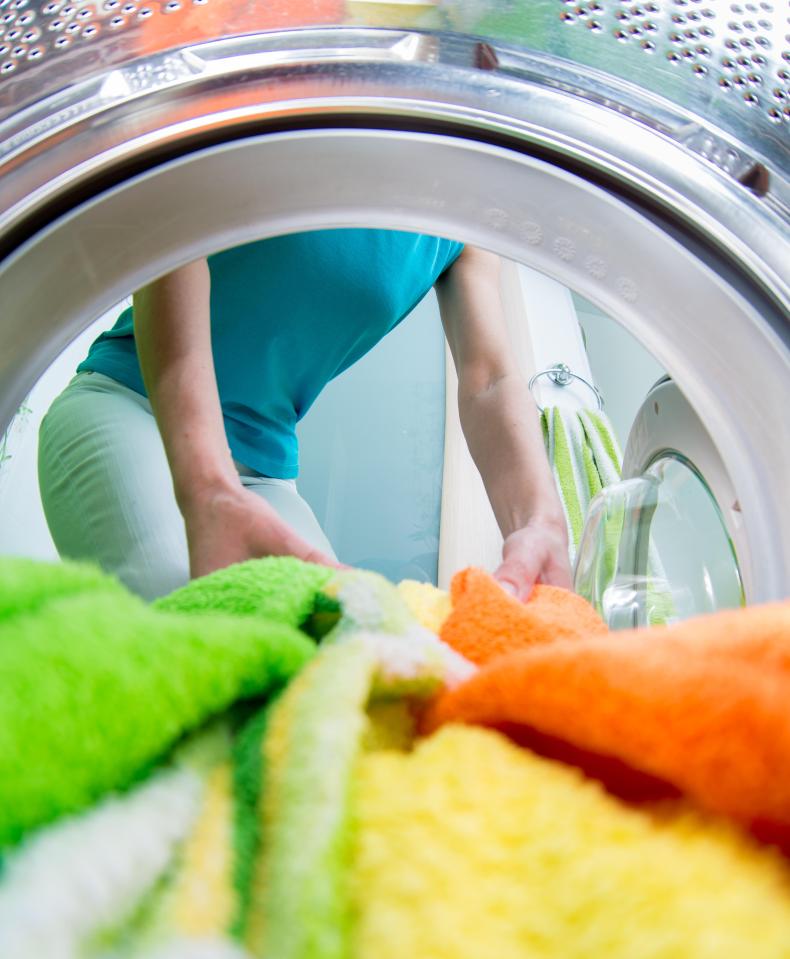 Woman loading colorful towels into a washing machine.