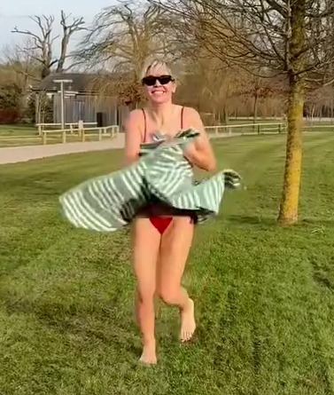 Woman in a red bikini running across a grassy field, holding a towel.