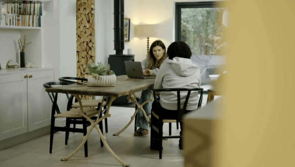Two women sitting at a table, looking at a laptop.