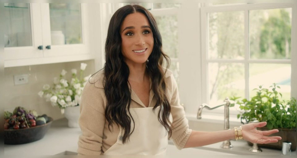 Meghan, Duchess of Sussex, in a kitchen, wearing an apron.