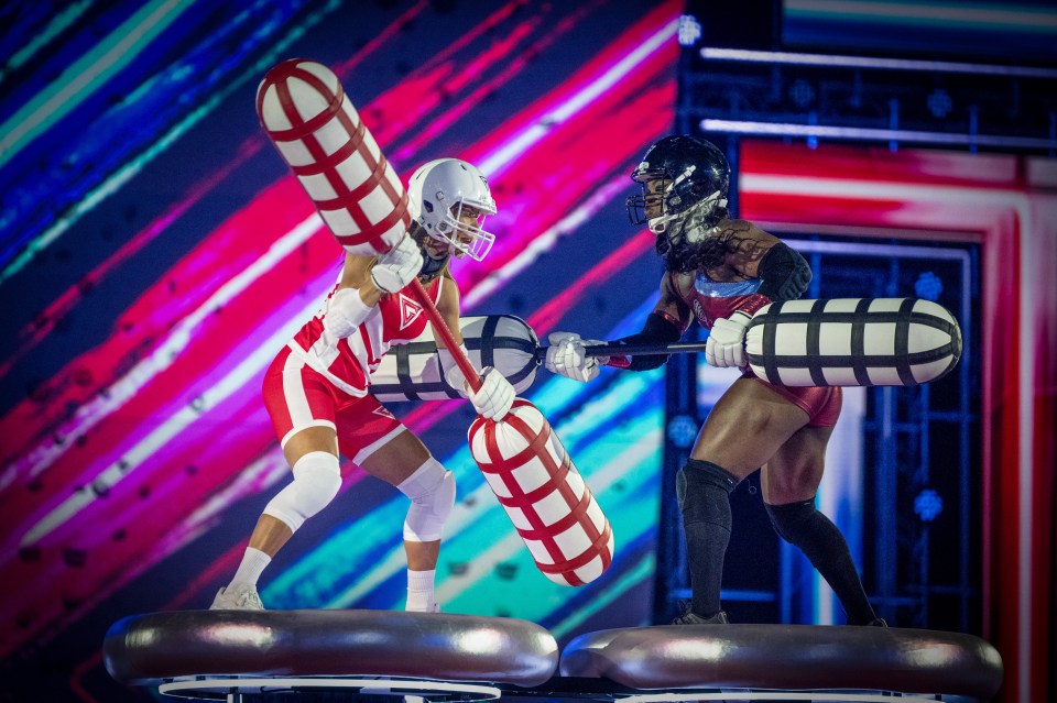 Two women gladiators compete in a battle using large padded poles.