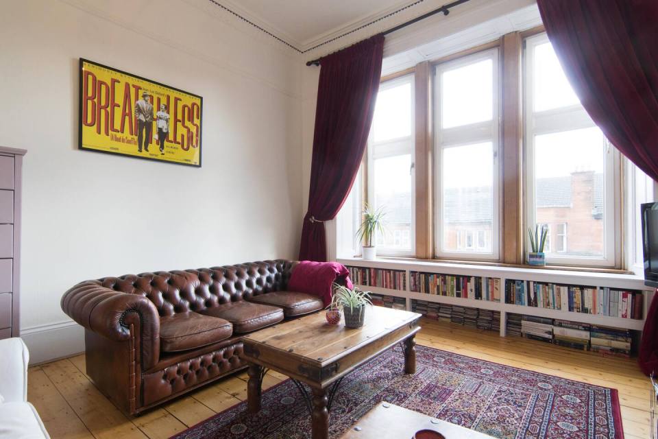 Living room with leather sofa, bookshelves, and large window.