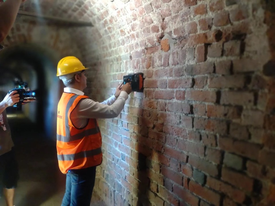A worker uses ground-penetrating radar on a brick wall in a tunnel.