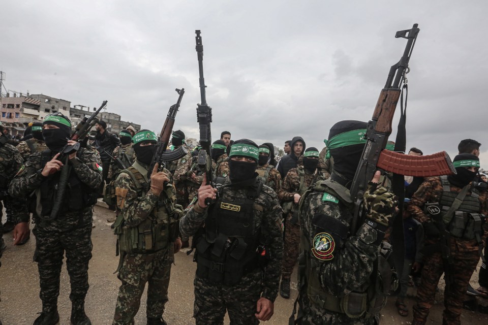 Hamas fighters carrying rifles at a hostage handover in Gaza.