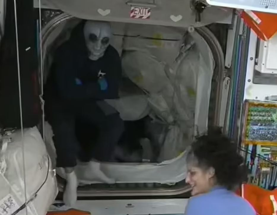 Astronaut greeting another astronaut aboard the International Space Station, one wearing an alien mask.