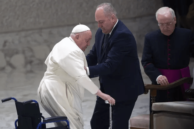 Pope Francis being assisted by a man while using a cane and wheelchair.