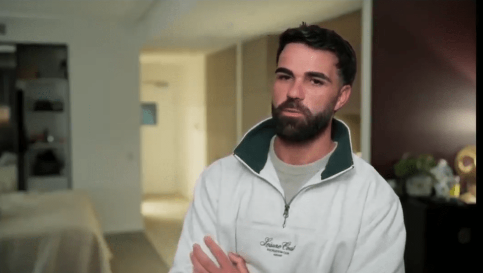 Man with beard in white zip-up sweatshirt.