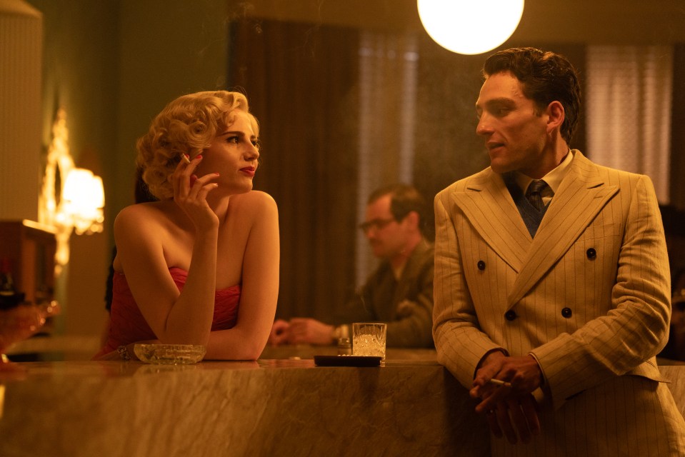 Still from *A Cruel Love: The Ruth Ellis Story* showing Lucy Boynton as Ruth Ellis and Laurie Davidson as David Blakely in a bar.