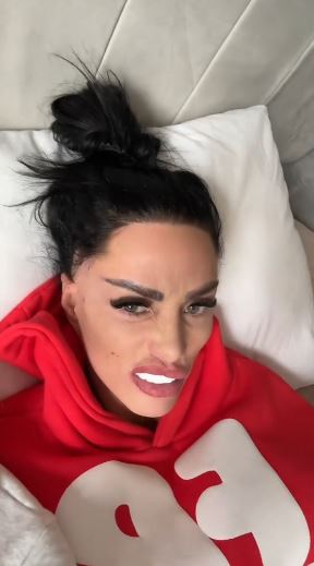 Katie Price in a red hoodie lying in bed.