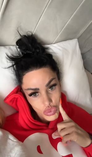 Katie Price in a red hoodie lying in bed.