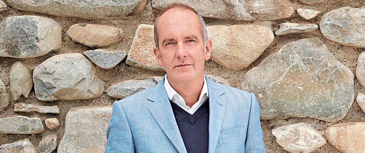 Portrait of Kevin McCloud in front of a stone wall.