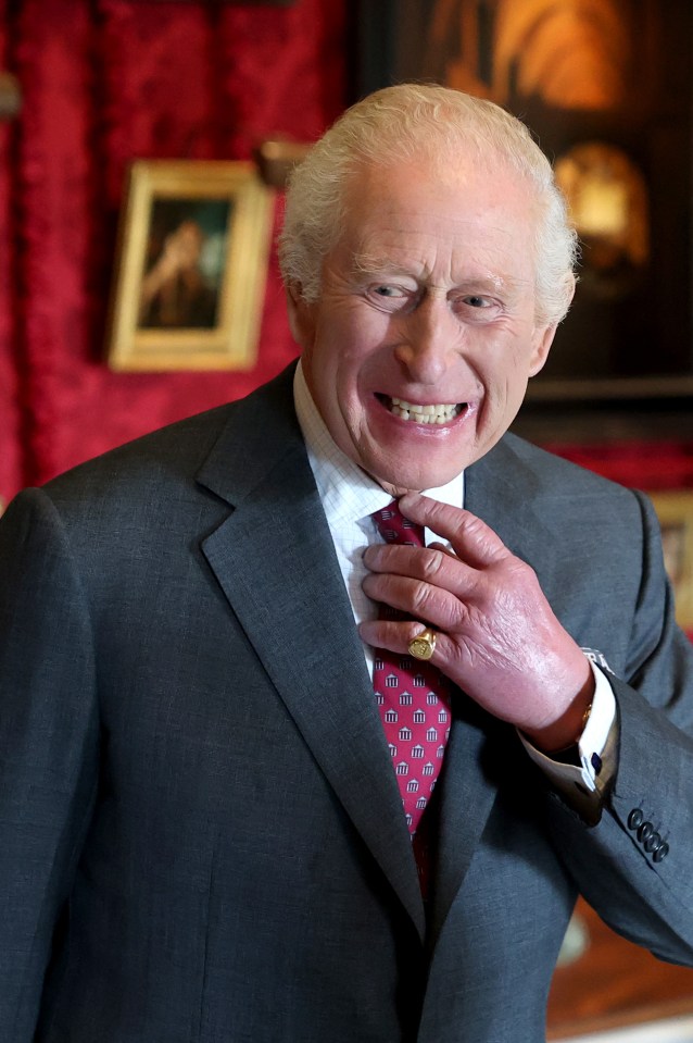 King Charles III smiles while adjusting his tie.