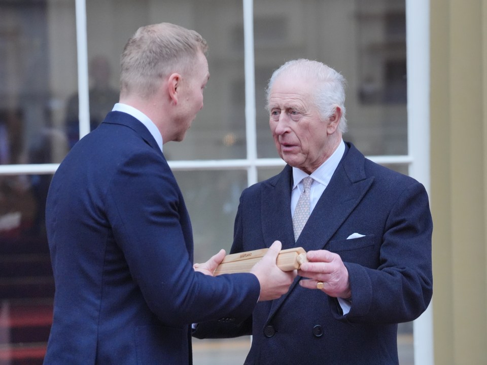 King Charles III receives a baton from Sir Chris Hoy at Buckingham Palace.