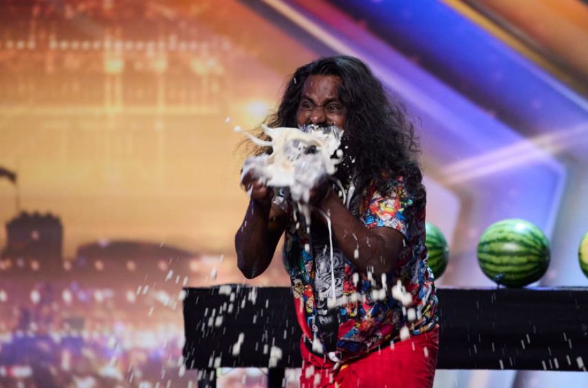 A man with long hair performs a messy act on stage, splattering a white substance.