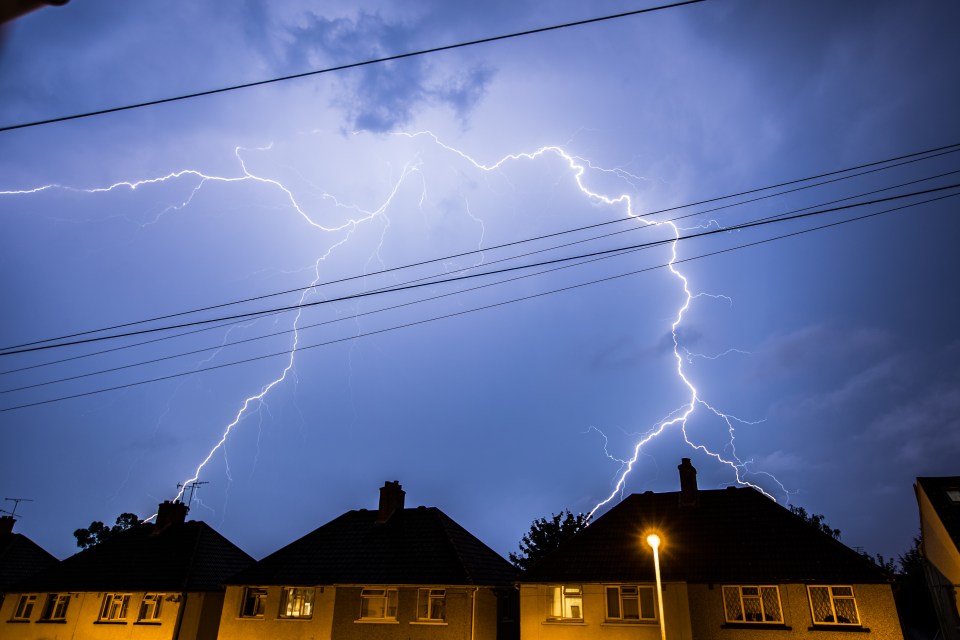 Lightning striking over houses at night.