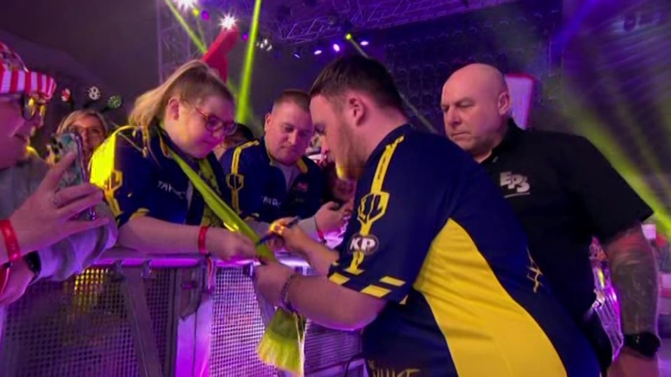 A man in a yellow and blue jersey signing autographs for fans.