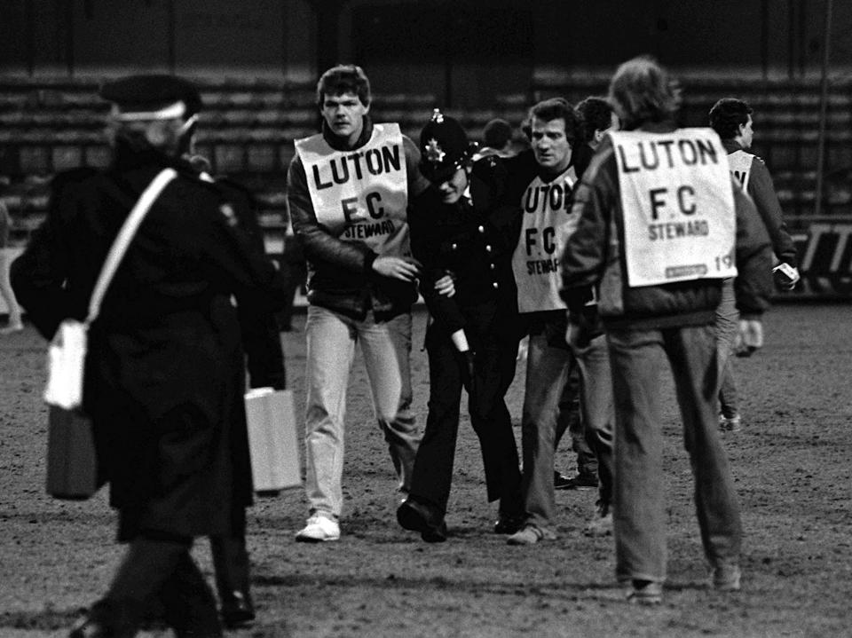 Black and white photo of a police officer escorting a man away at a soccer match.