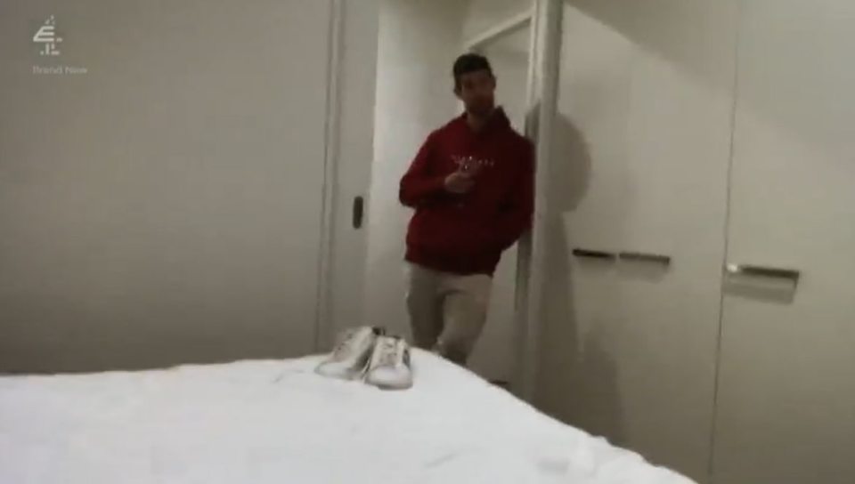 Man in red sweatshirt standing in bedroom.