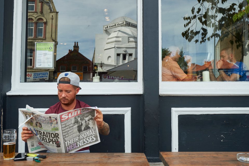 Man reading The Sun newspaper outside a pub.