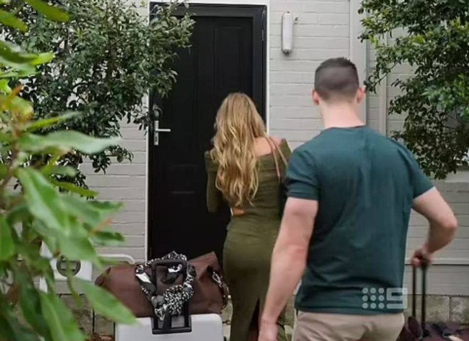 A woman and a man arrive at a house with luggage.
