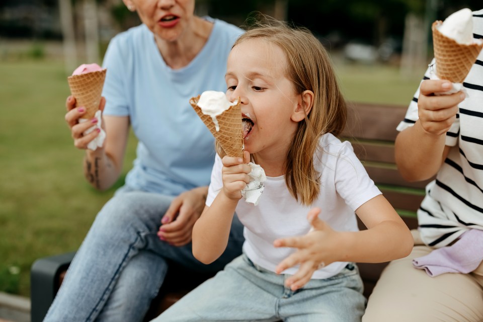 Three generations of women enjoy ice cream cones together on a park bench.