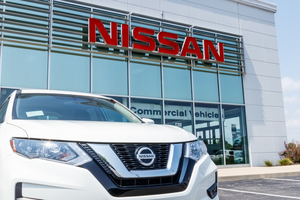 White Nissan SUV parked in front of a Nissan dealership.
