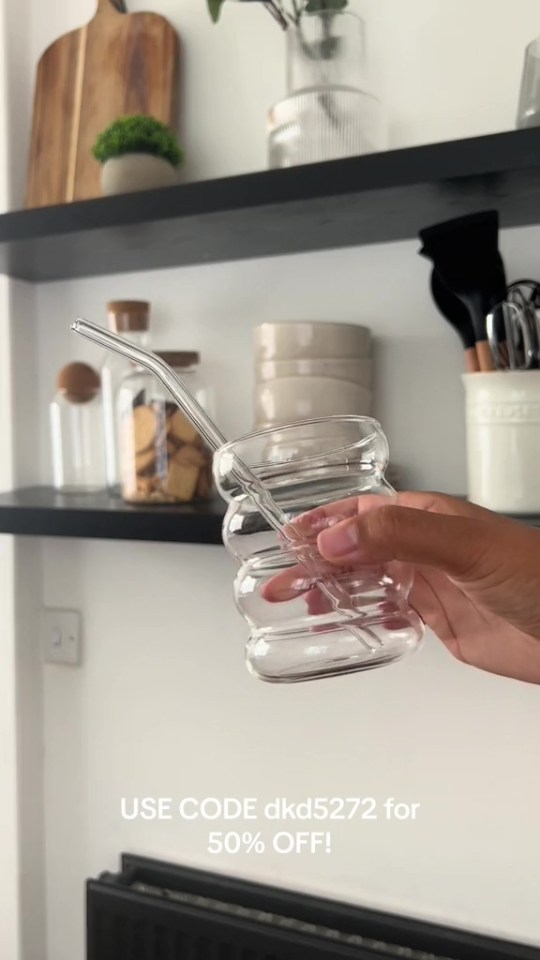 Hand holding a clear glass with a glass straw.