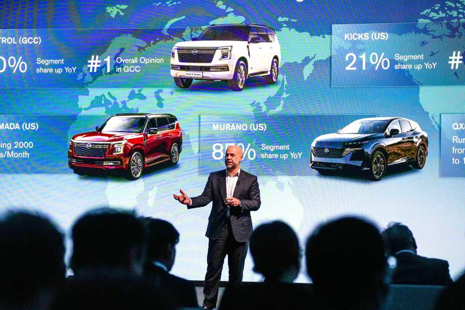 A man presenting Nissan sales data on a screen showing various Nissan vehicles.