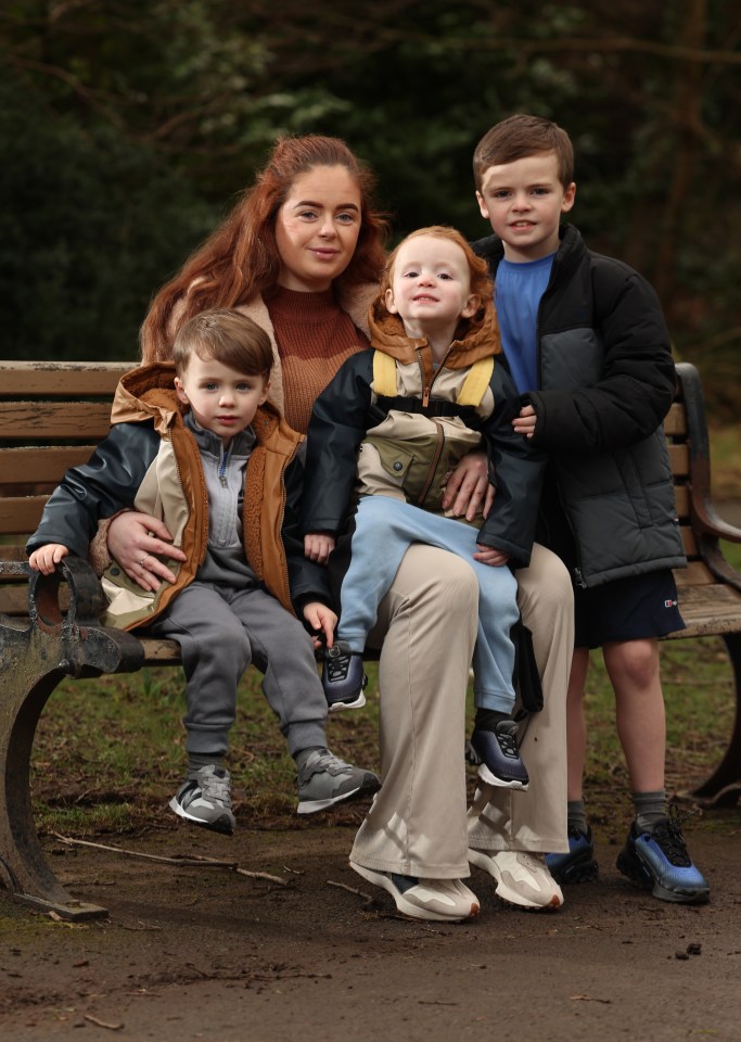 A mother and her three children sitting on a park bench.