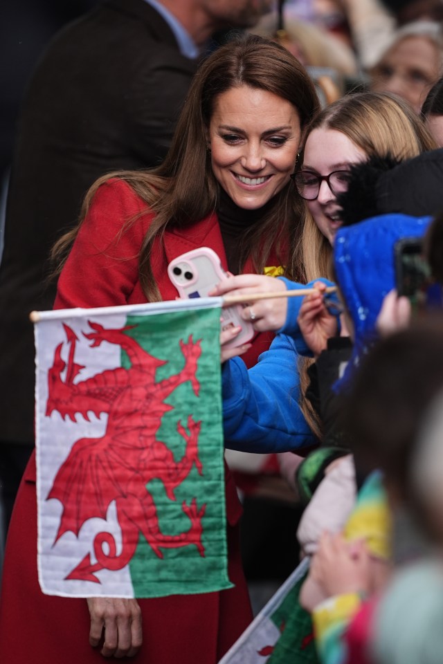 The Princess of Wales greets well-wishers and takes a selfie with them while holding a Welsh flag.