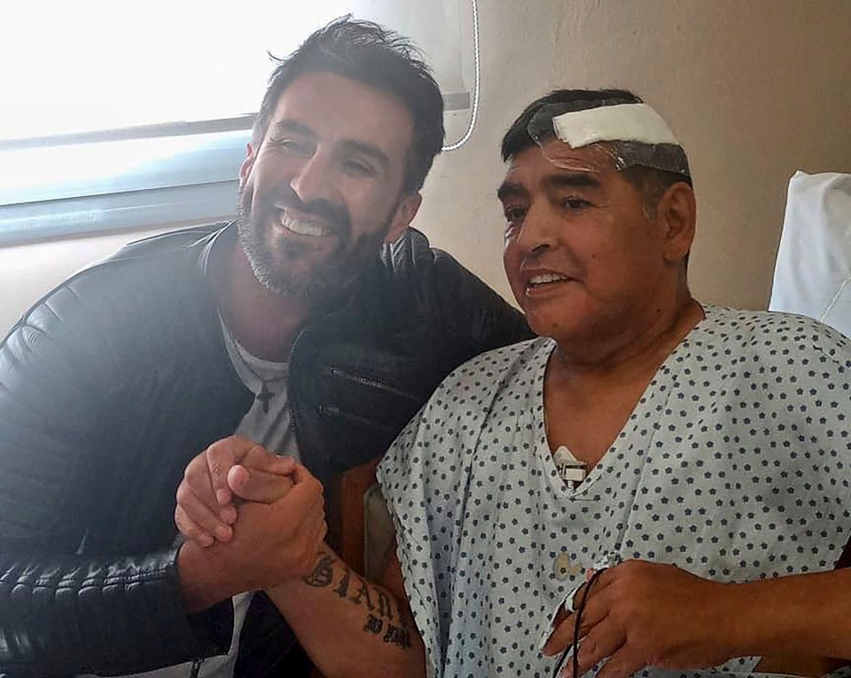 Diego Maradona in a hospital bed holding hands with a man.