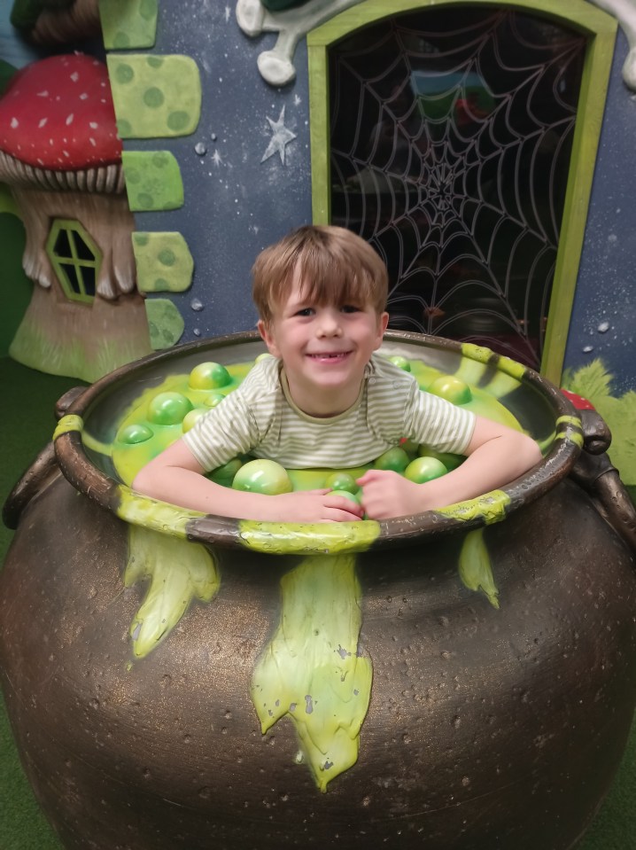 Boy sitting in a large cauldron filled with green balls.