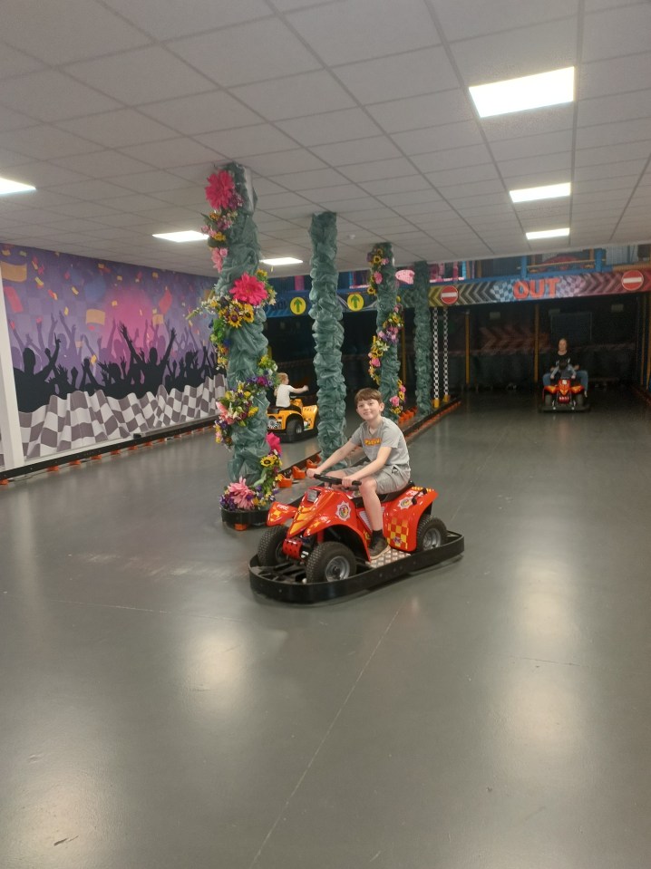 Boy driving a red kiddie ATV in an indoor race track.