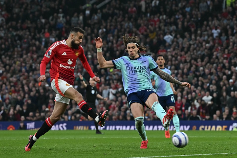 A soccer player in a light blue uniform kicks the ball while a player in a red uniform defends.