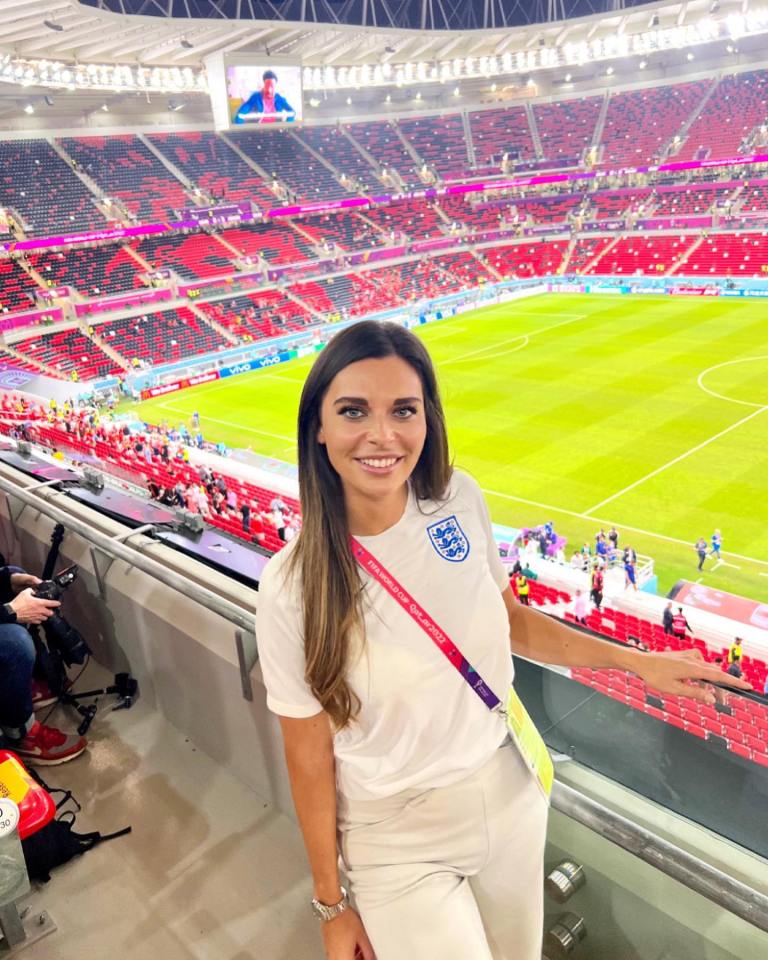 Woman in a white England soccer jersey stands in a stadium.