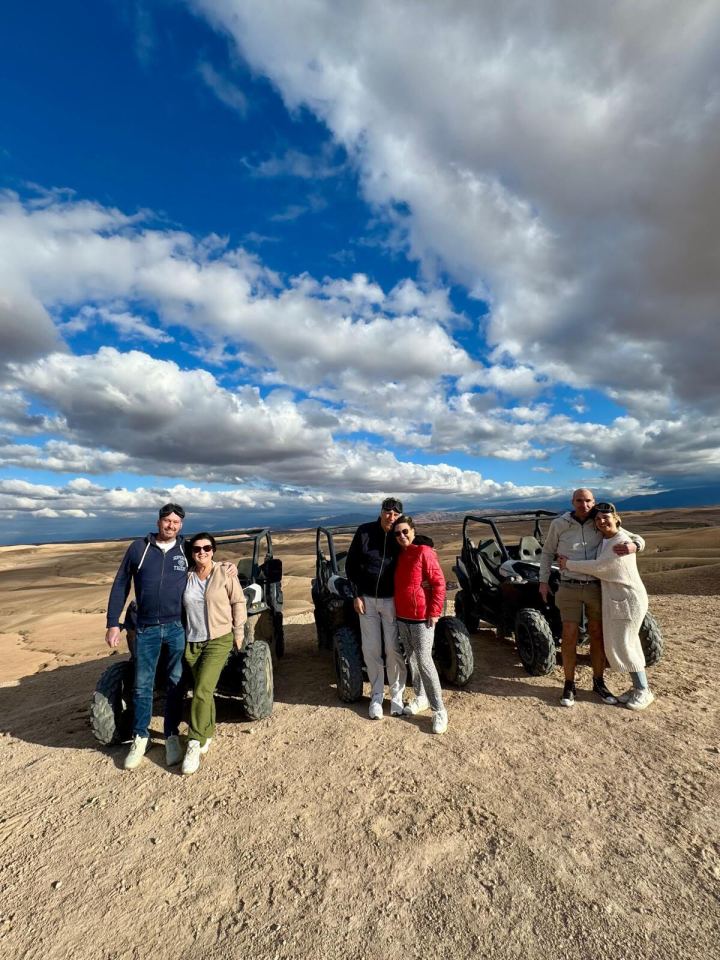 Group of people posing with ATVs in a desert landscape.