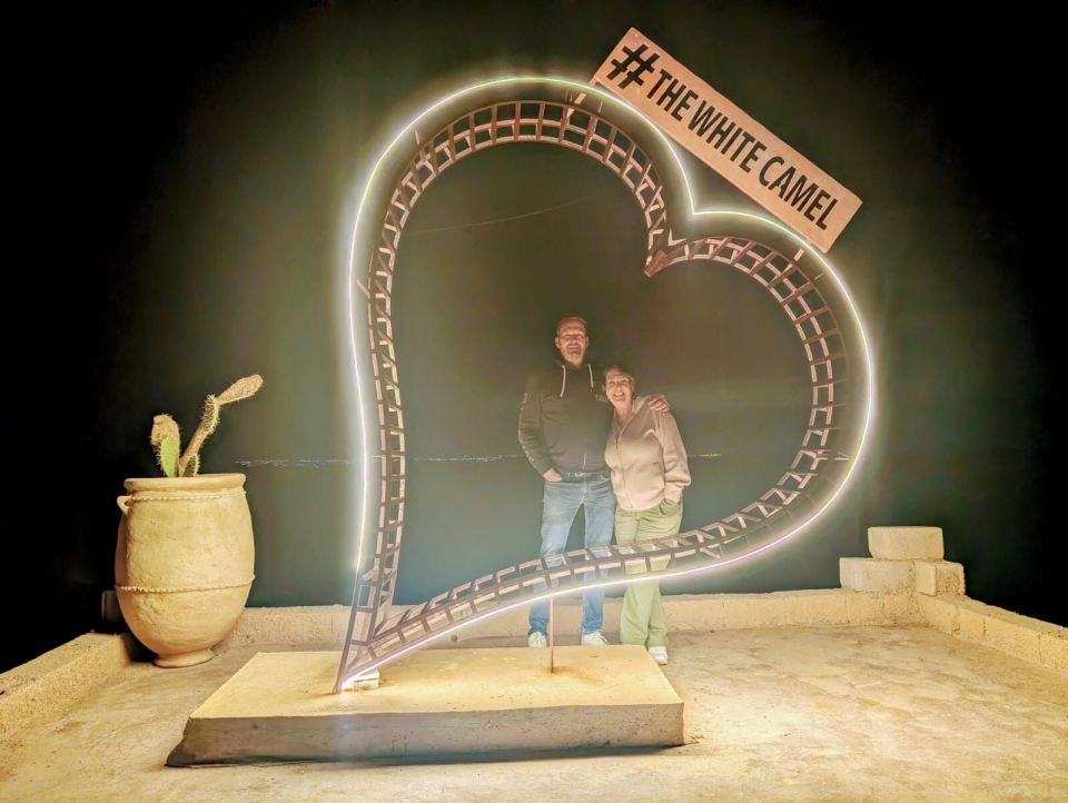 Couple standing in front of illuminated heart-shaped structure at night.