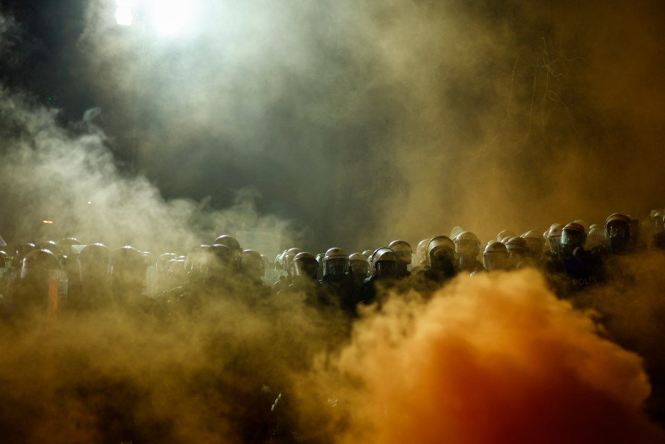 Riot police obscured by smoke at a demonstration.