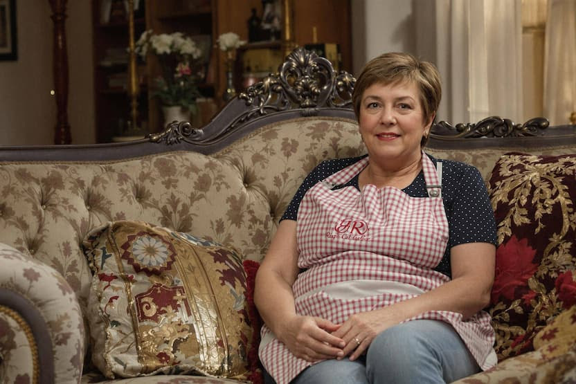 Woman in apron sitting on ornate couch.