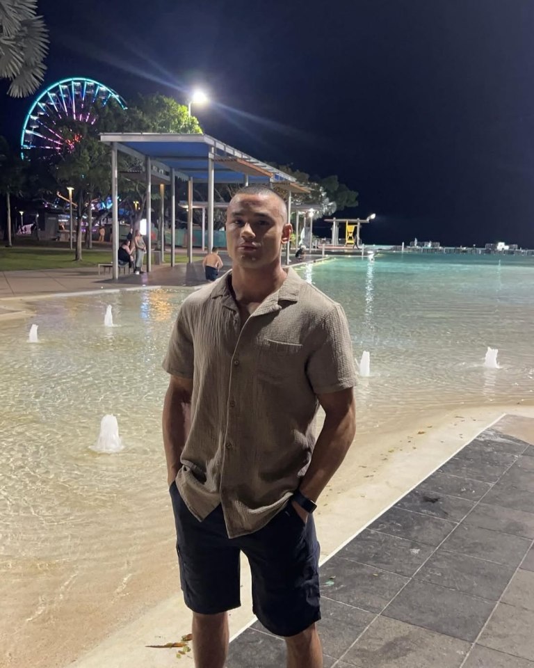 Man in tan shirt and dark shorts standing by a pool at night.