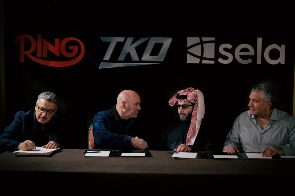 Four men sitting at a table signing documents.  The Ring, TKO, and Sela logos are visible on the wall behind them.